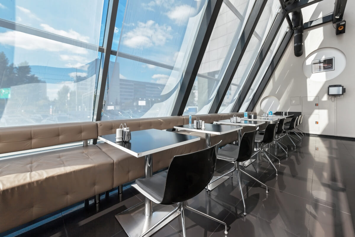 Nowoczesne wnętrze restauracji z chromowanymi podstawami do stołów i dużymi oknami.