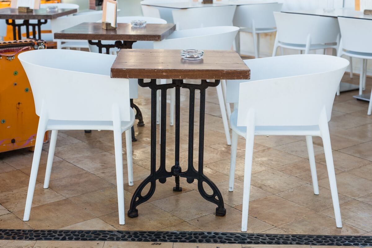 Stolik z drewnianym blatem oparty na metalowej podstawie do stołów, otoczony białymi krzesłami.