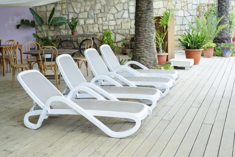 Na drewnianym tarasie ustawiono białe leżaki basenowe plastikowe.
