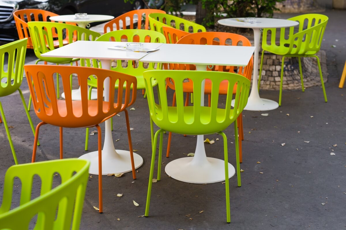 Kolorowe krzesła otaczają stoły ogrodowe plastikowe na tarasie.
